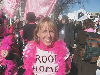 activist medea benjamin wearing a pink boa and a shirt that says 'troops home now'